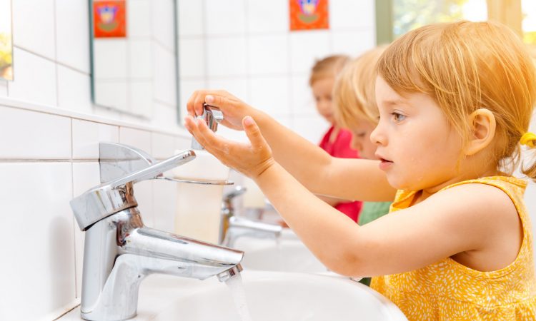 Child in kindergarten washing her hands in bathroom